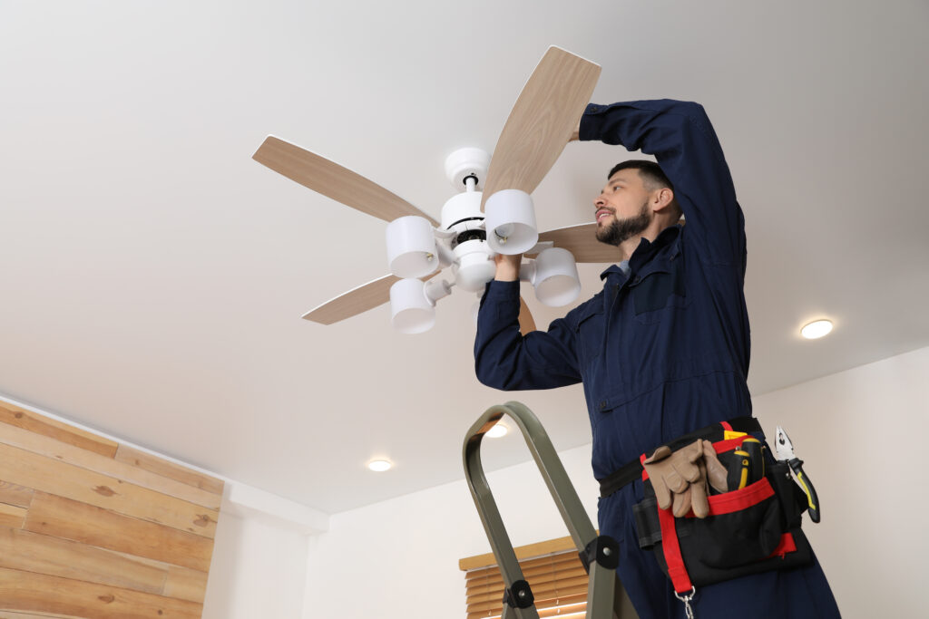 Technician fixing a ceiling fan for proper balance and optimal air circulation and efficiency.