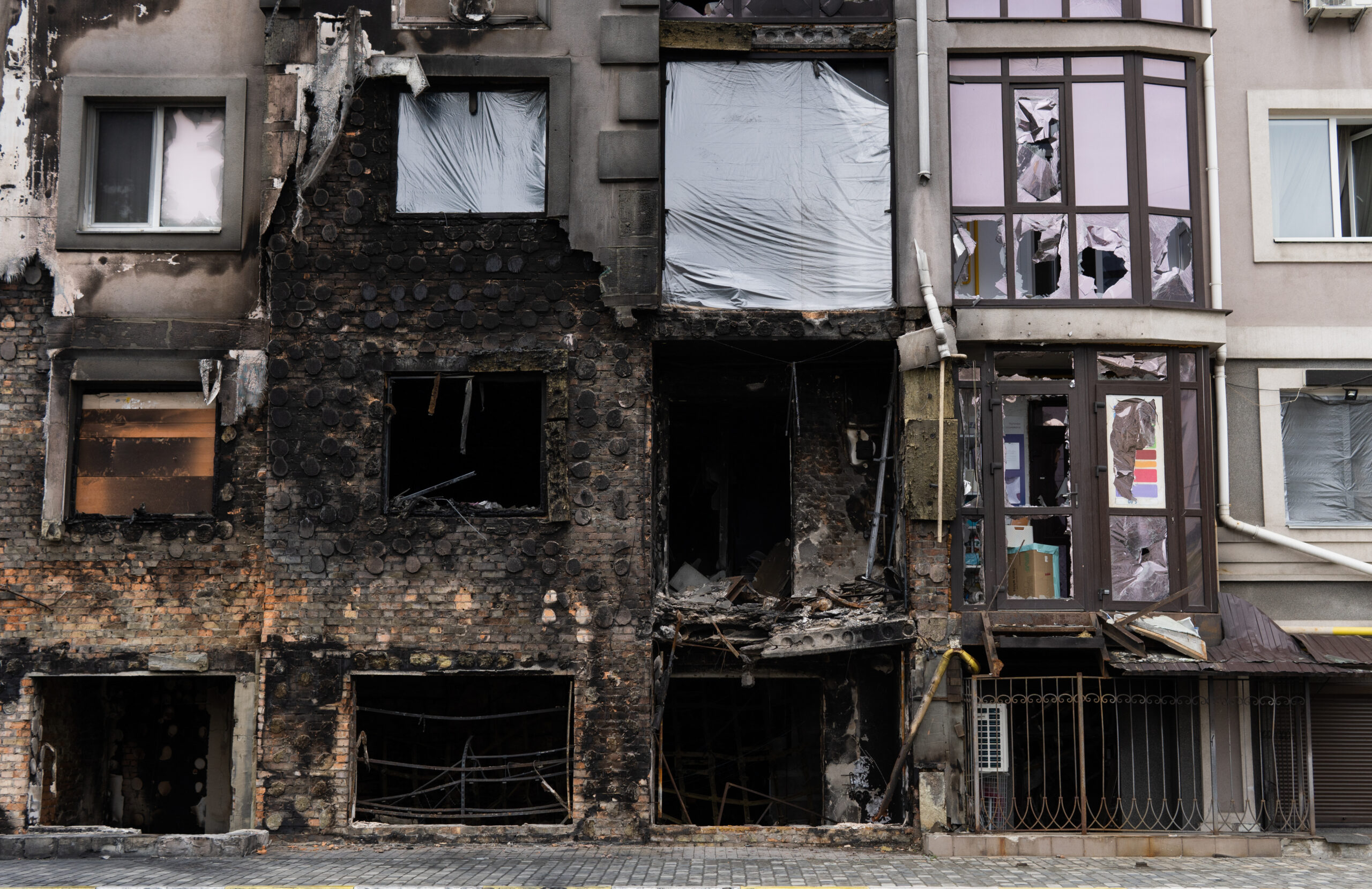 Windows of an apartment building showing extensive fire damage, with broken glass and soot-stained frames