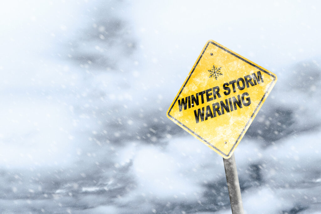 A winter storm warning sign stands with heavy snowfall in the background, emphasizing the importance of following a winter storm preparedness checklist to stay safe and ready for severe weather conditions.